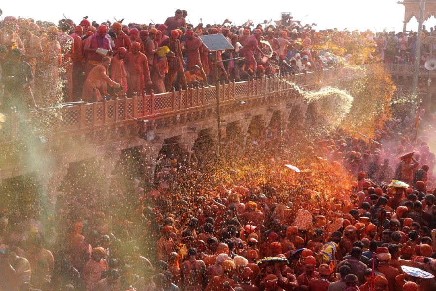 A large crowd of people in a temple square are doused with colored water by people standing above.