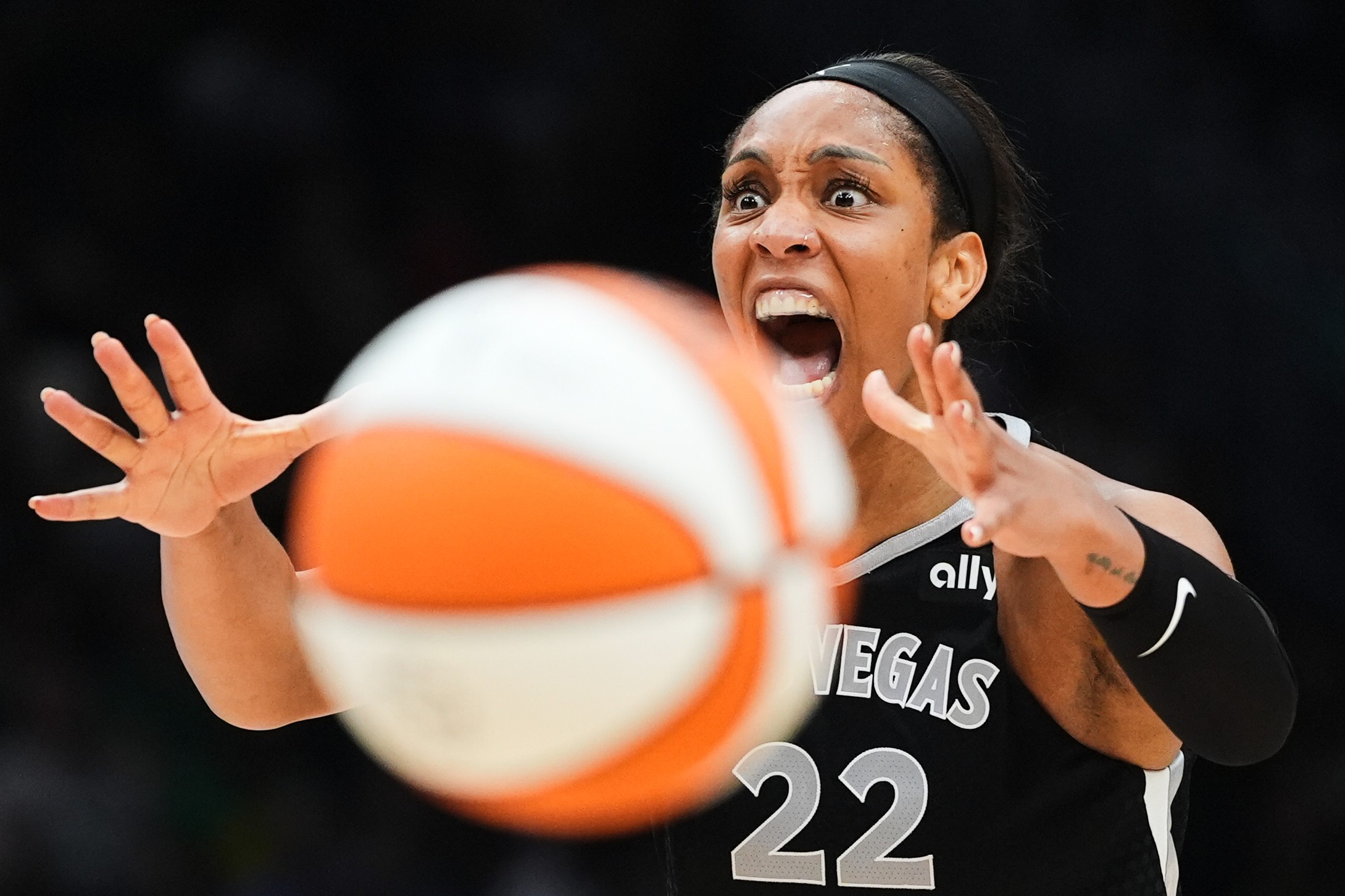 A basketball player reacts, their mouth wide open, as an out-of-focus basketball passes in front of the camera.