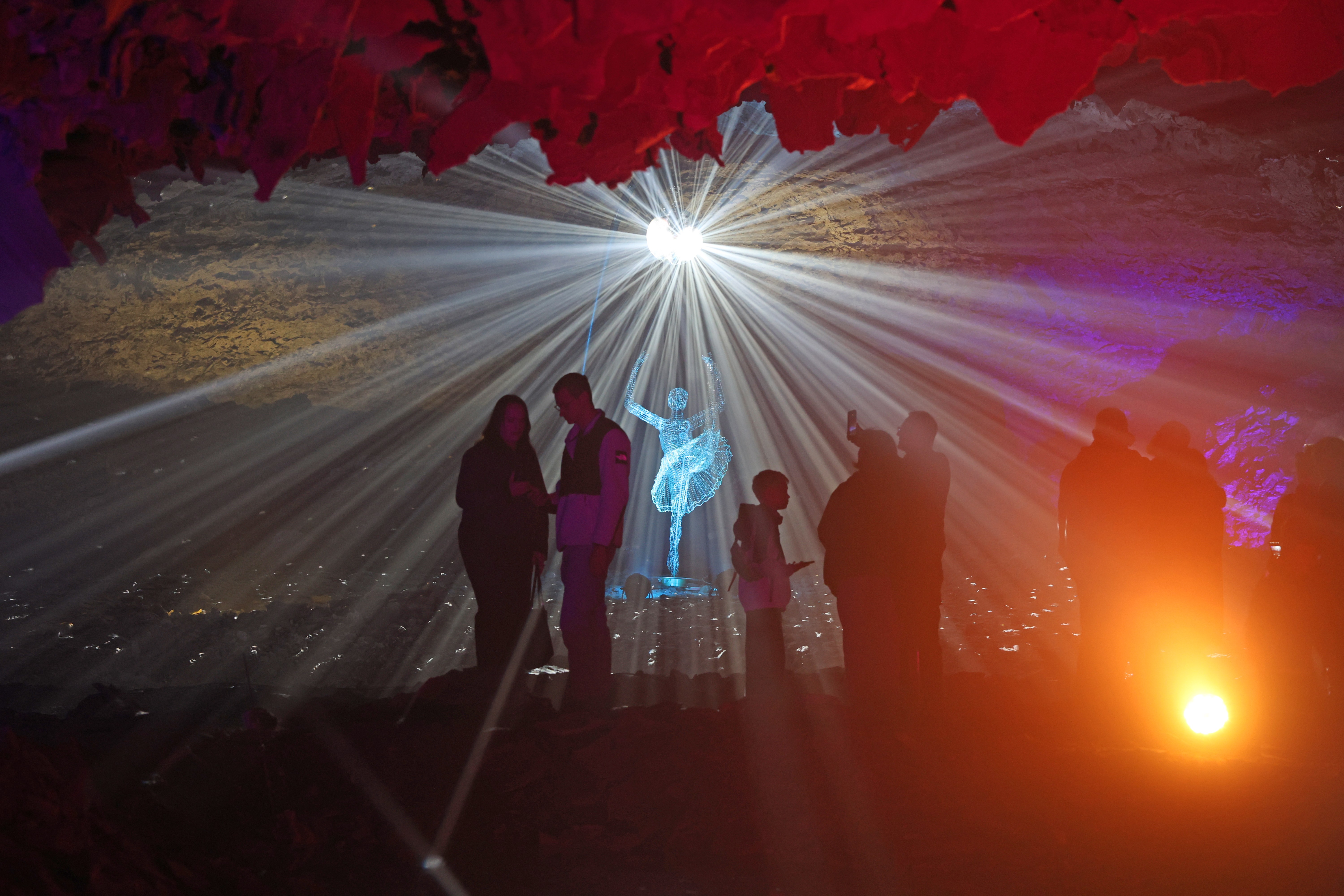People walk through a cave amid a light show.