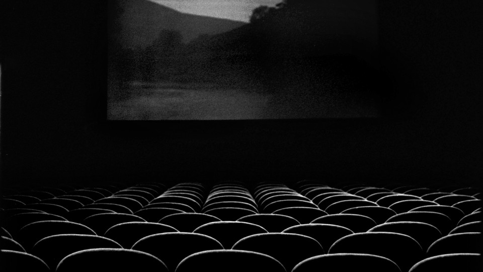 A black and white image of an empty movie theatre with a scenic location on screen