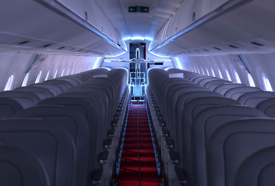 A specialized robot with broad arms carrying ultraviolet lights moves down the aisle of an aircraft.