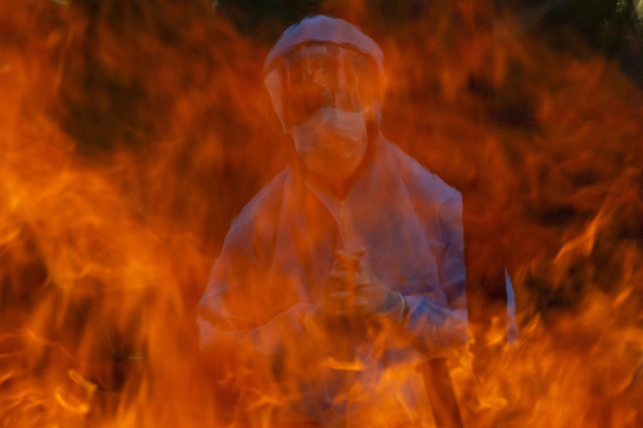 A person in protective gear is seen standing behind tall flames.