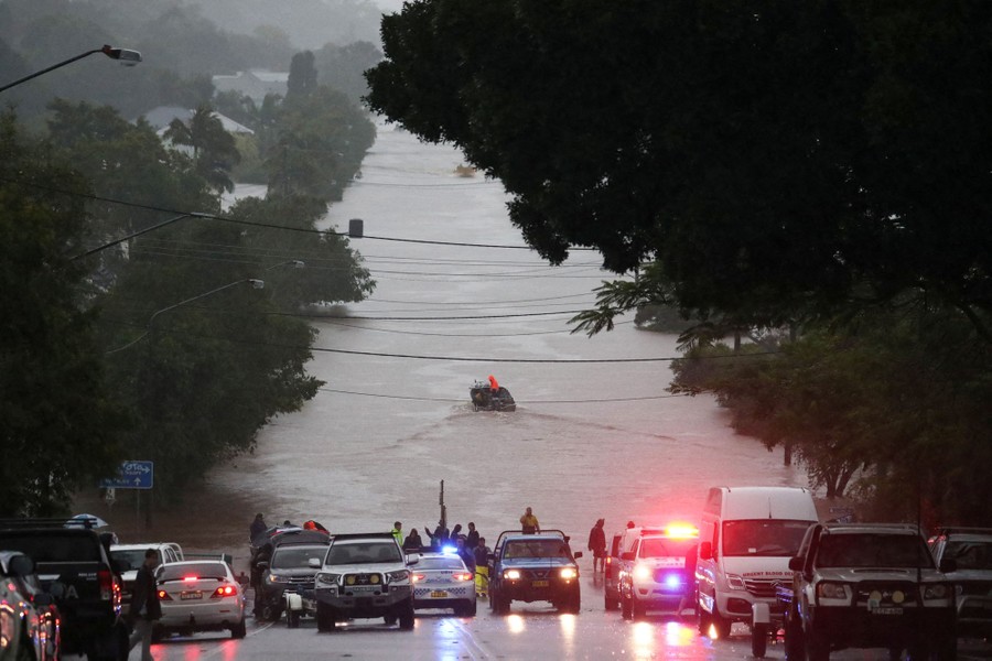 About a dozen vehicles sit parked on a road alongside a large flooded portion of land.