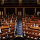 An overview shot of the House of Representatives, with members wearing suits or blazers and sitting scattered throughout the rows of desks