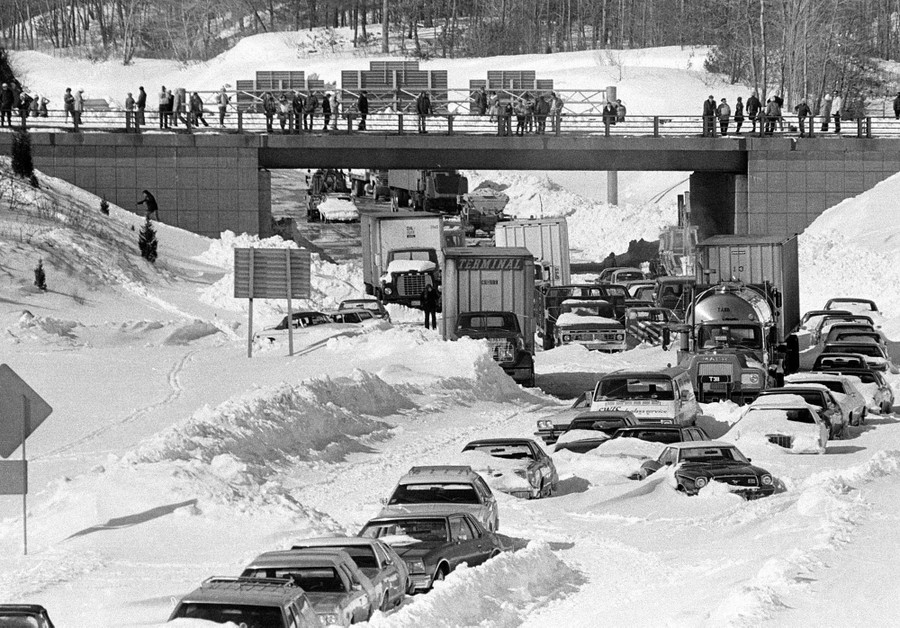 Many cars and trucks sit buried in deep snow on a highway.