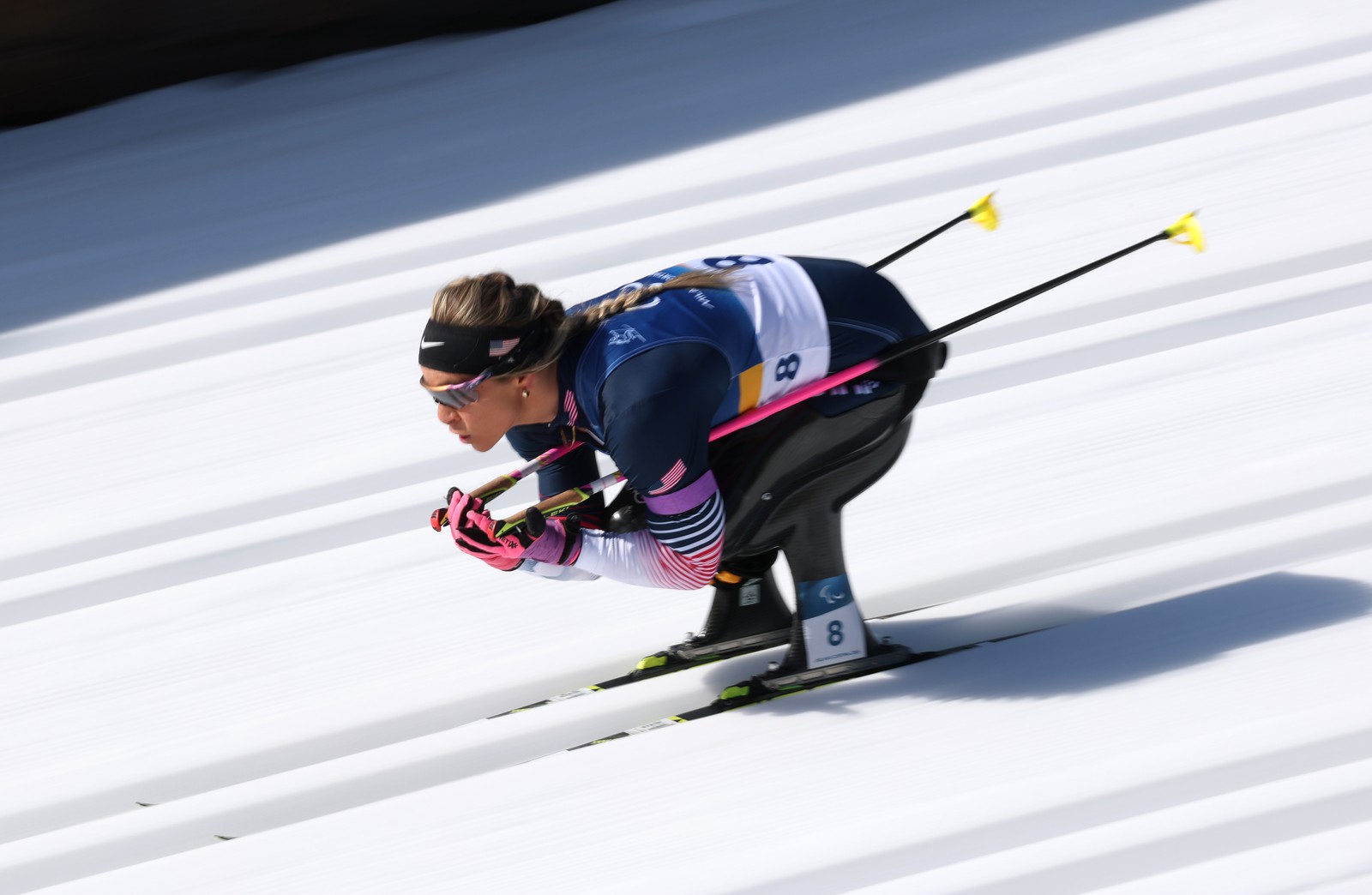 A seated skier tucks low, speeding down a track, their motion partly blurred.