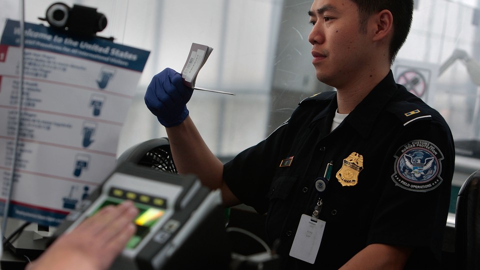 A traveler is fingerprinted while a border agent checks his paperwork.