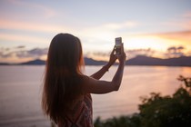 A woman takes a photo of a sunset.