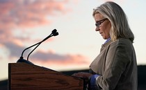 A profile photograph of Liz Cheney standing at a podium, speaking about her future political plans after her 2022 primary defeat