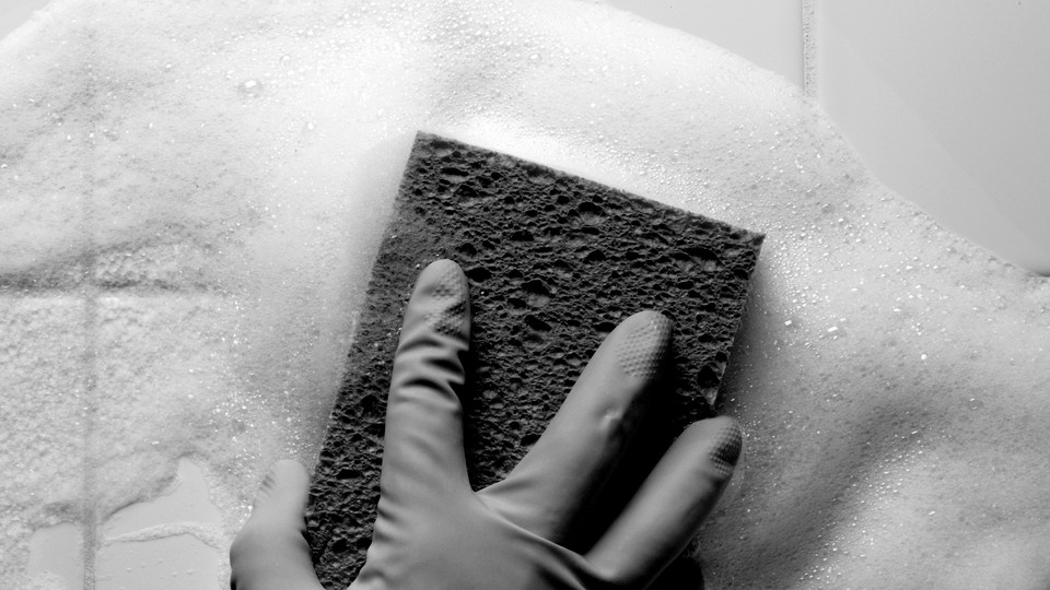 A gloved hand using a sponge to clean a tiled wall