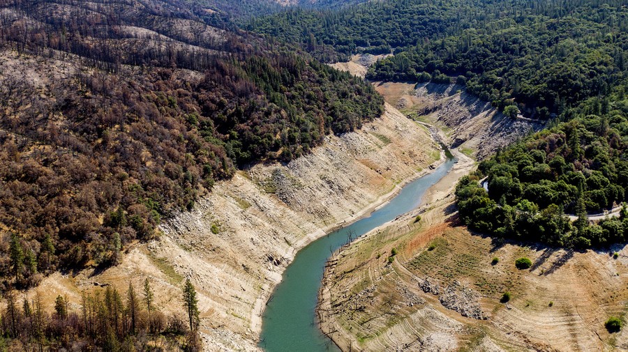Dry and scorched vegetation stand along the steep banks of a drying reservoir.