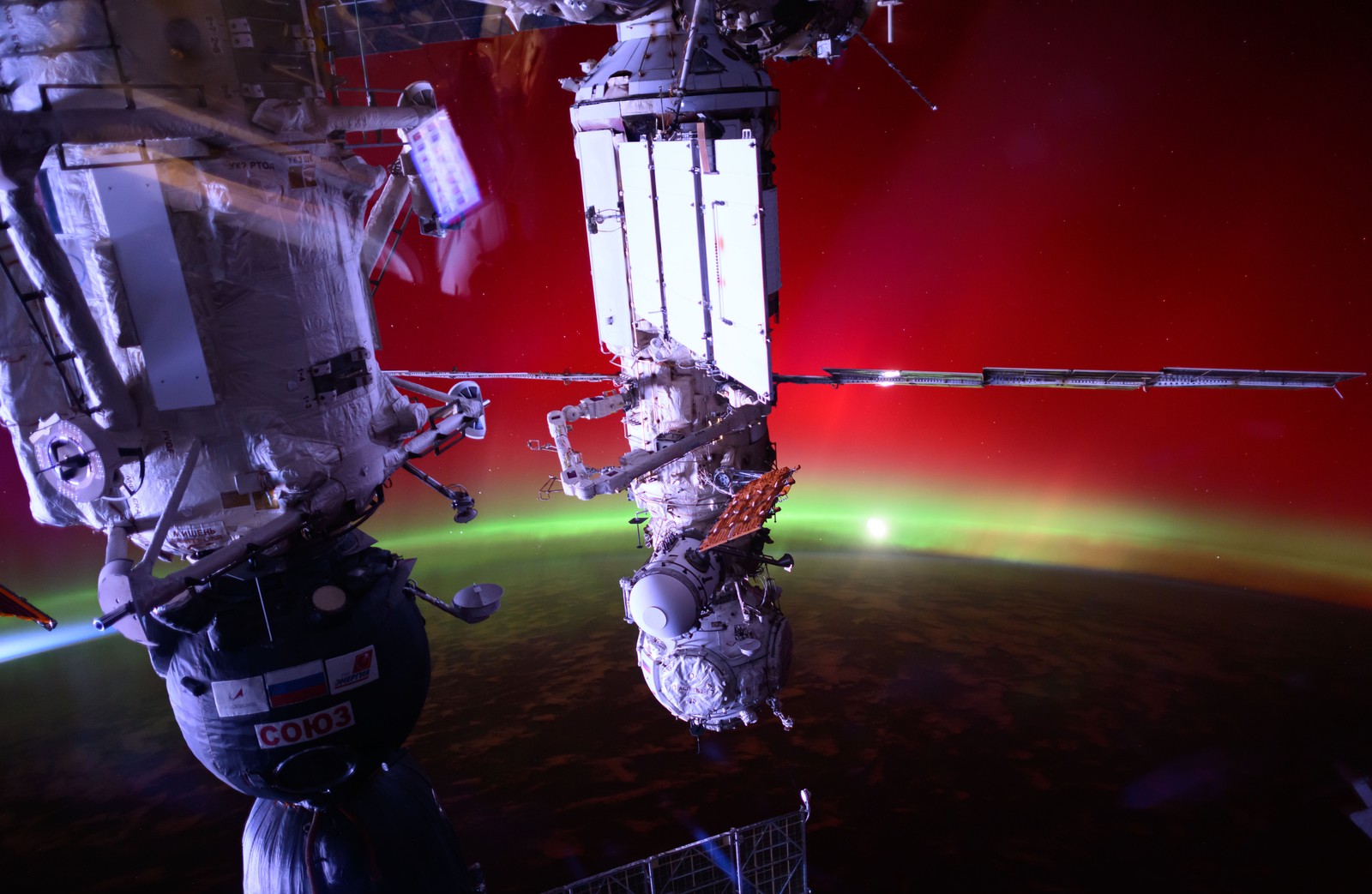 An aurora glows beyond docked spacecraft and components of the International Space Station.