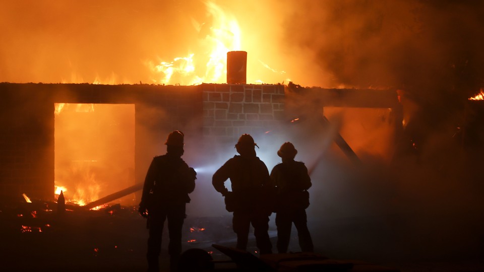 Firefighters stand in front of a burning house.