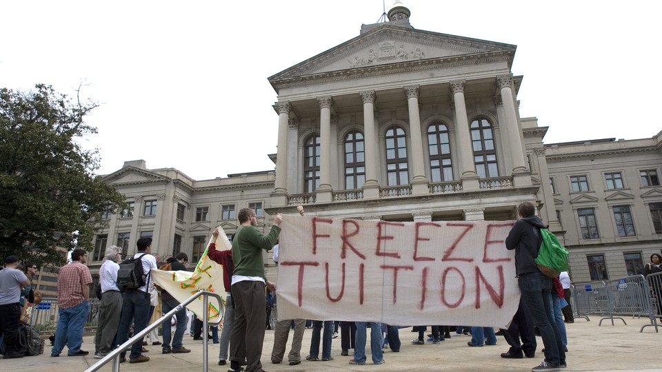 Students and alumni hold a sign that reads "Freeze Tuition."