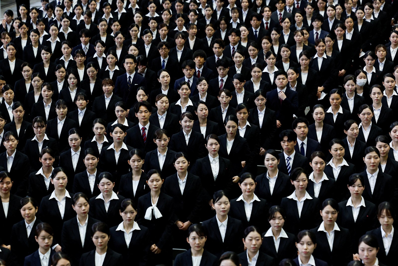 Dozens of people wearing white shirts and dark jackets stand in rows during an initiation ceremony.