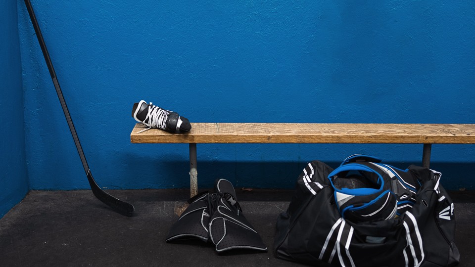 Hockey gear near and on a wooden bench in front of a blue wall