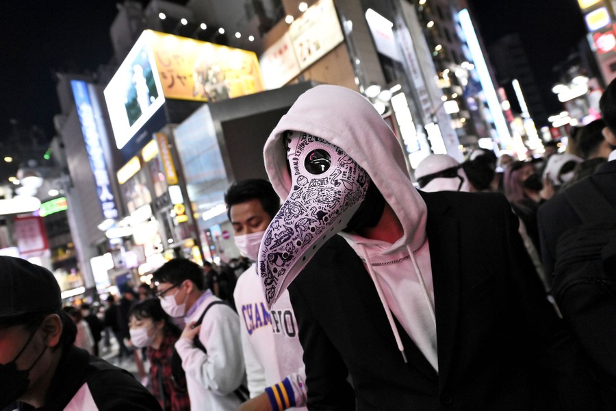A person wears a stylized bird/plague-doctor mask in a crowd.