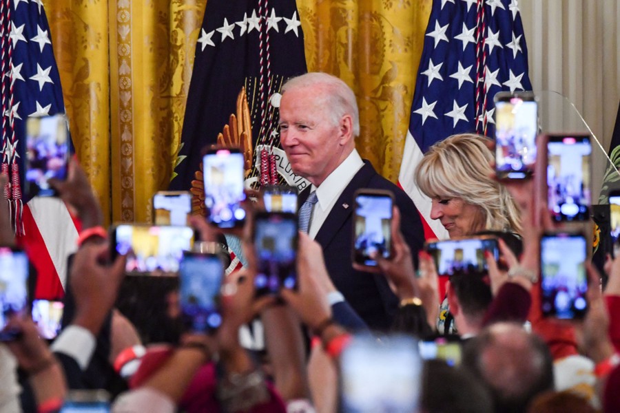 A crowd of people hold up their mobile devices, taking photographs of President Biden and his wife, Jill Biden.