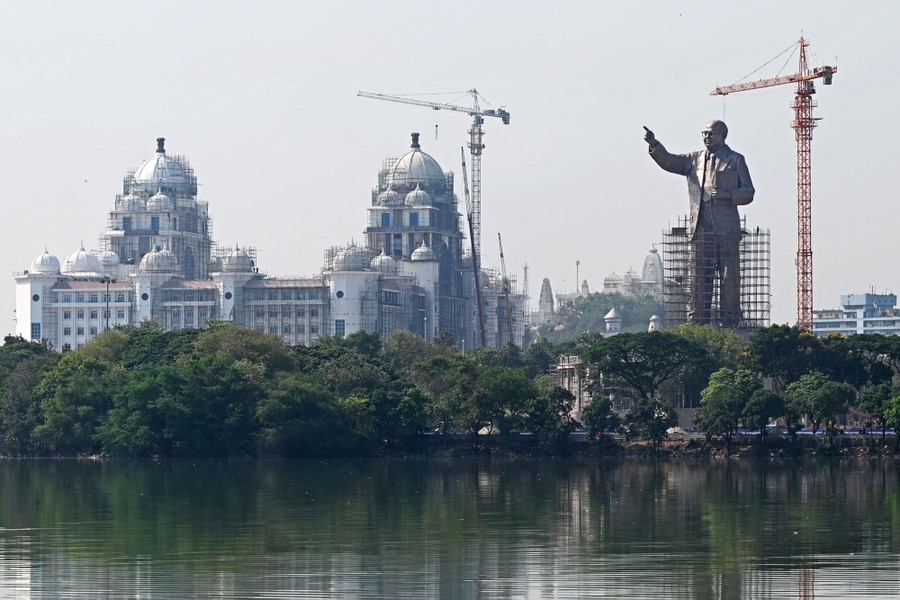 A 125-foot-tall bronze statue of a man stands near a body of water and several buildings.