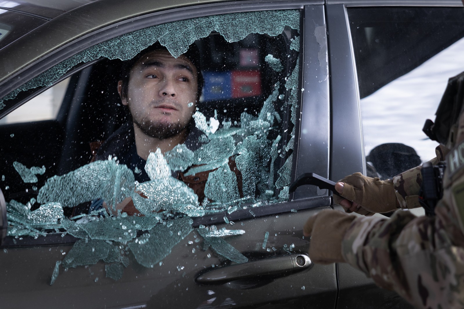 The smashed glass of a car window falls after being broken by a federal agent, while the driver looks out the window.