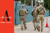 A color photograph of uniformed National Guard troops carrying guns while walking down a sidewalk in Washington, D.C.