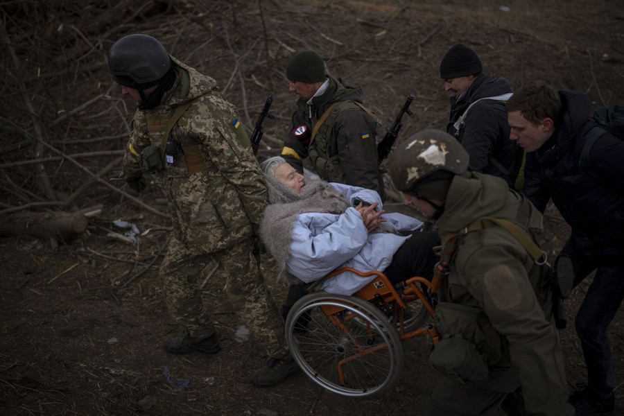 Several soldiers and militiamen carry a woman in a wheelchair.