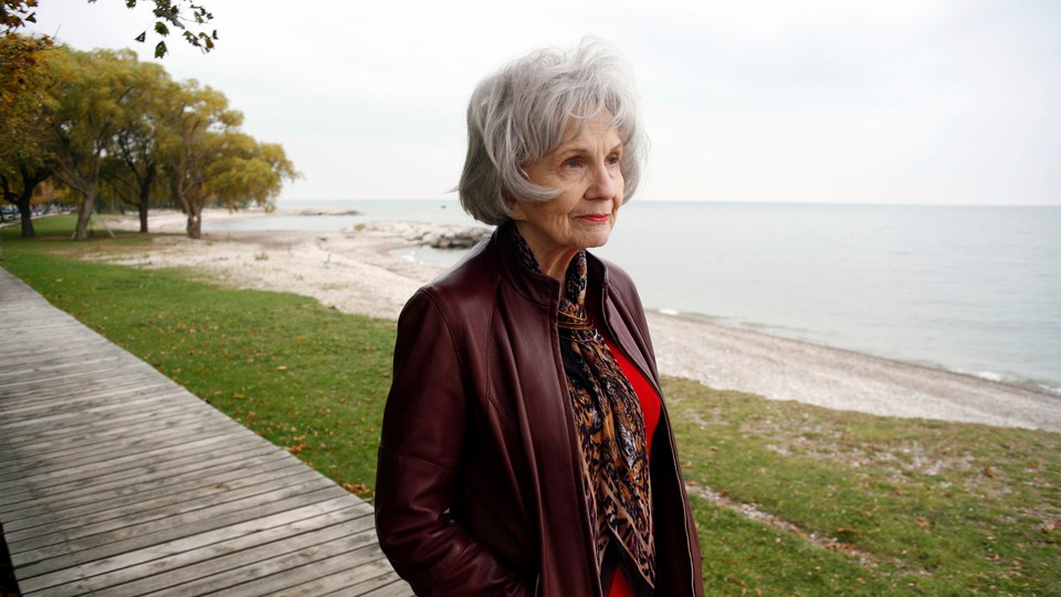 Alice Munro walks in front of a river and looks off to the right