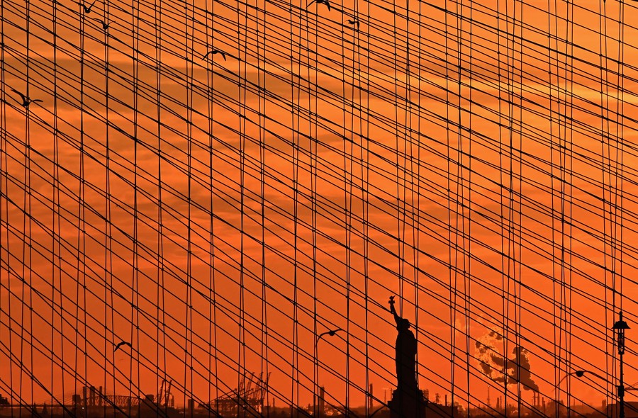 A distant view of the Statue of Liberty, seen through bridge cables