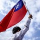 Man holding the Taiwan flag up in the air, in front of a blue sky