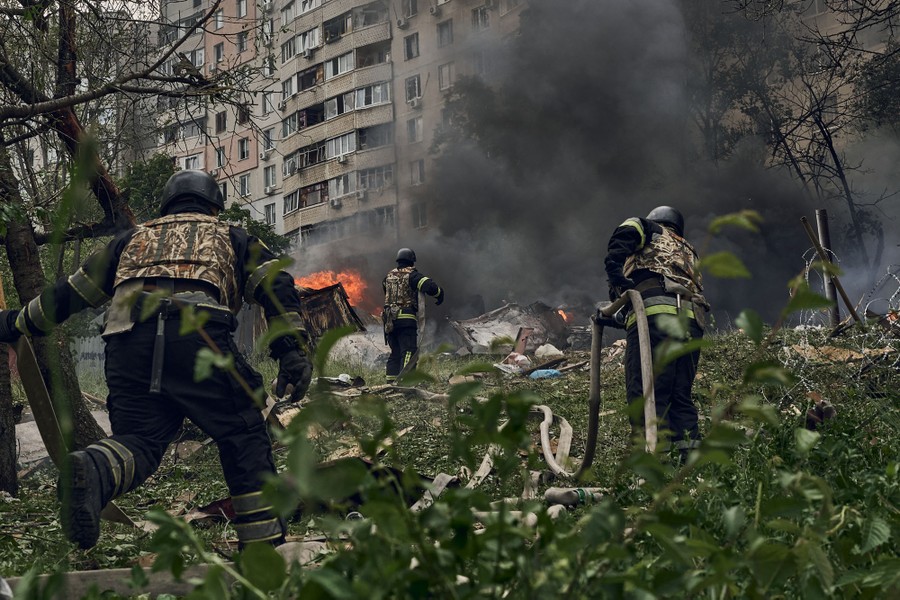 Several firefighters scramble over downed tree limbs and wreckage to spray water on a fire following a missile attack.