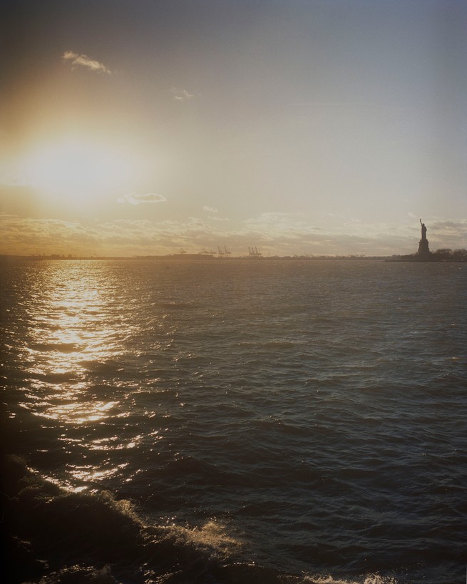 Sunlight reflects off the water across from the Statue of LIberty