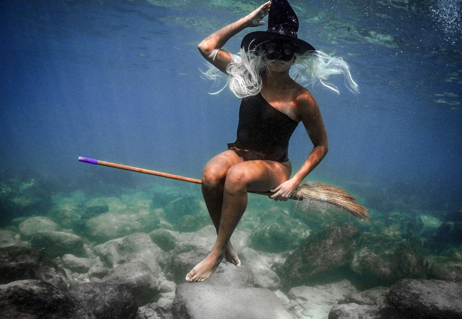 A woman dressed as a witch is photographed underwater, "riding" on a broom.