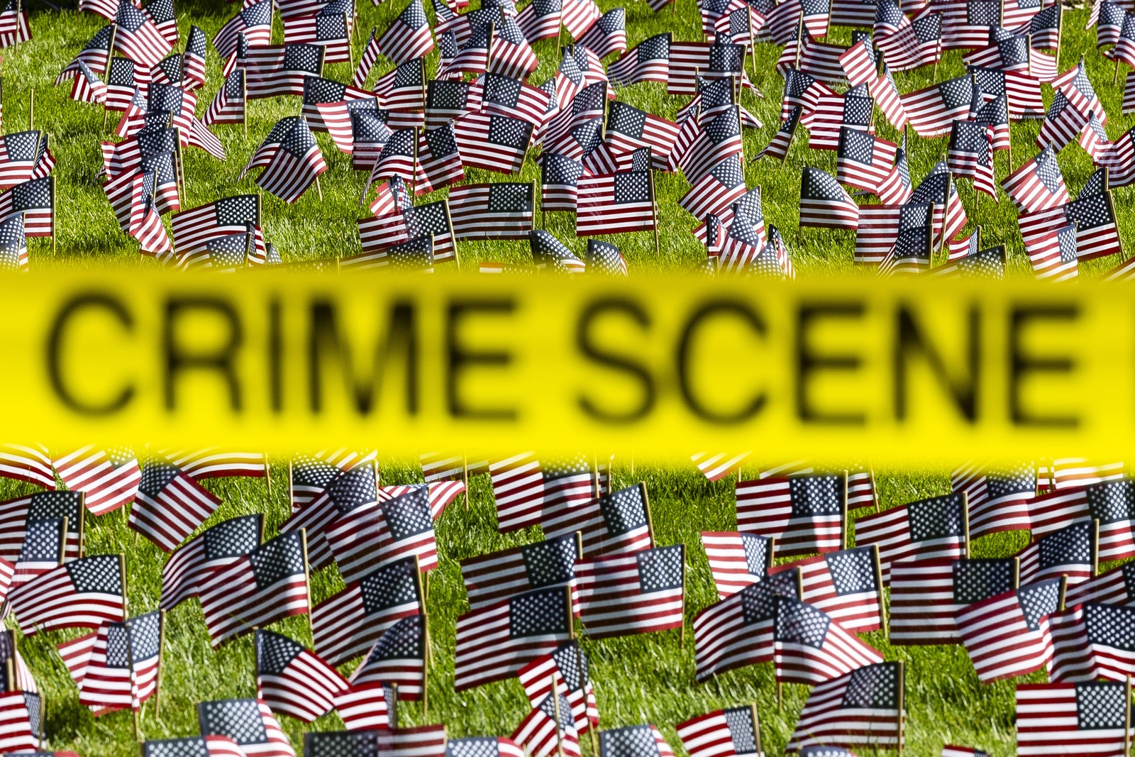 Yellow tape that reads 'Crime Scene' is stretched out in front of a lawn covered by dozens of small American flags.
