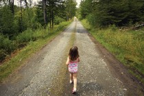 a little girl in a pink and bathing suit walks on a path in the woods