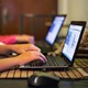 Two sets of hands typing on two black computers 