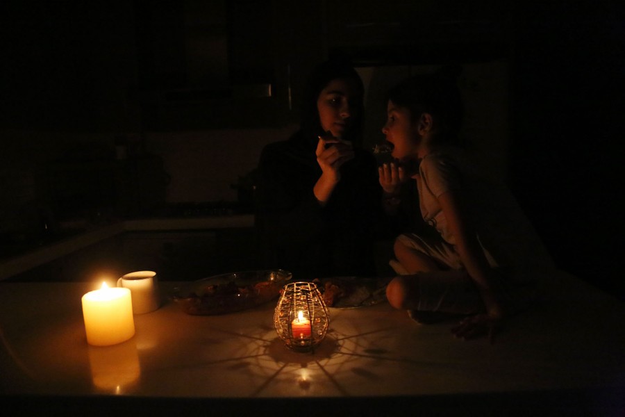 A woman and child share food in a dark kitchen lit by candles.