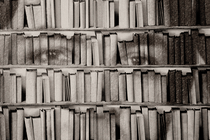 black and white photo of a man looking out from a bookshelf