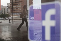 People walk past a Facebook logo on a shop window