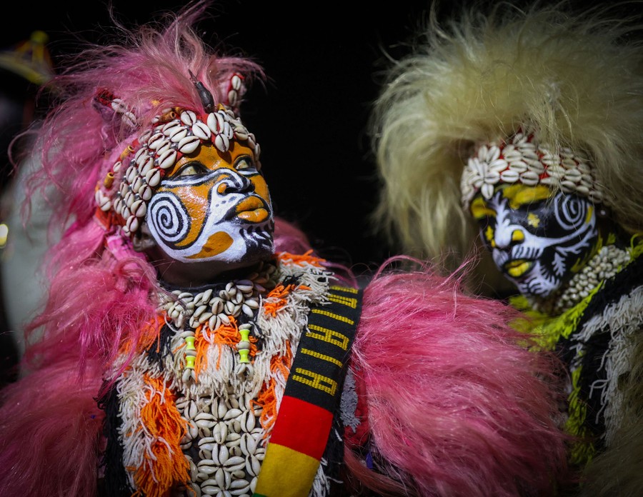 Performers in traditional costumes and elaborate face paint dance at a carnival.