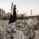 A veiled Iranian art student holds a country flag while standing on symbolic debris of a destroyed building as she performs in an anti-war conceptual play at a square in downtown Tehran, Iran