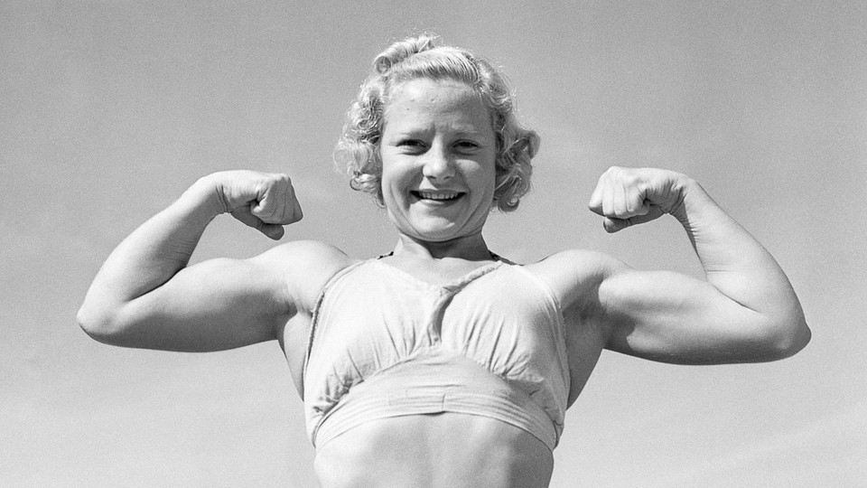 A black-and-white photo of a young woman in a sports bra showing off large biceps