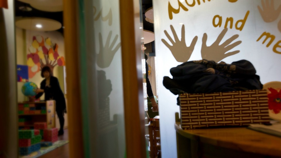 A teacher arranges a globe in a classroom. A sign reads "mommy and me" with handprints around the text. 