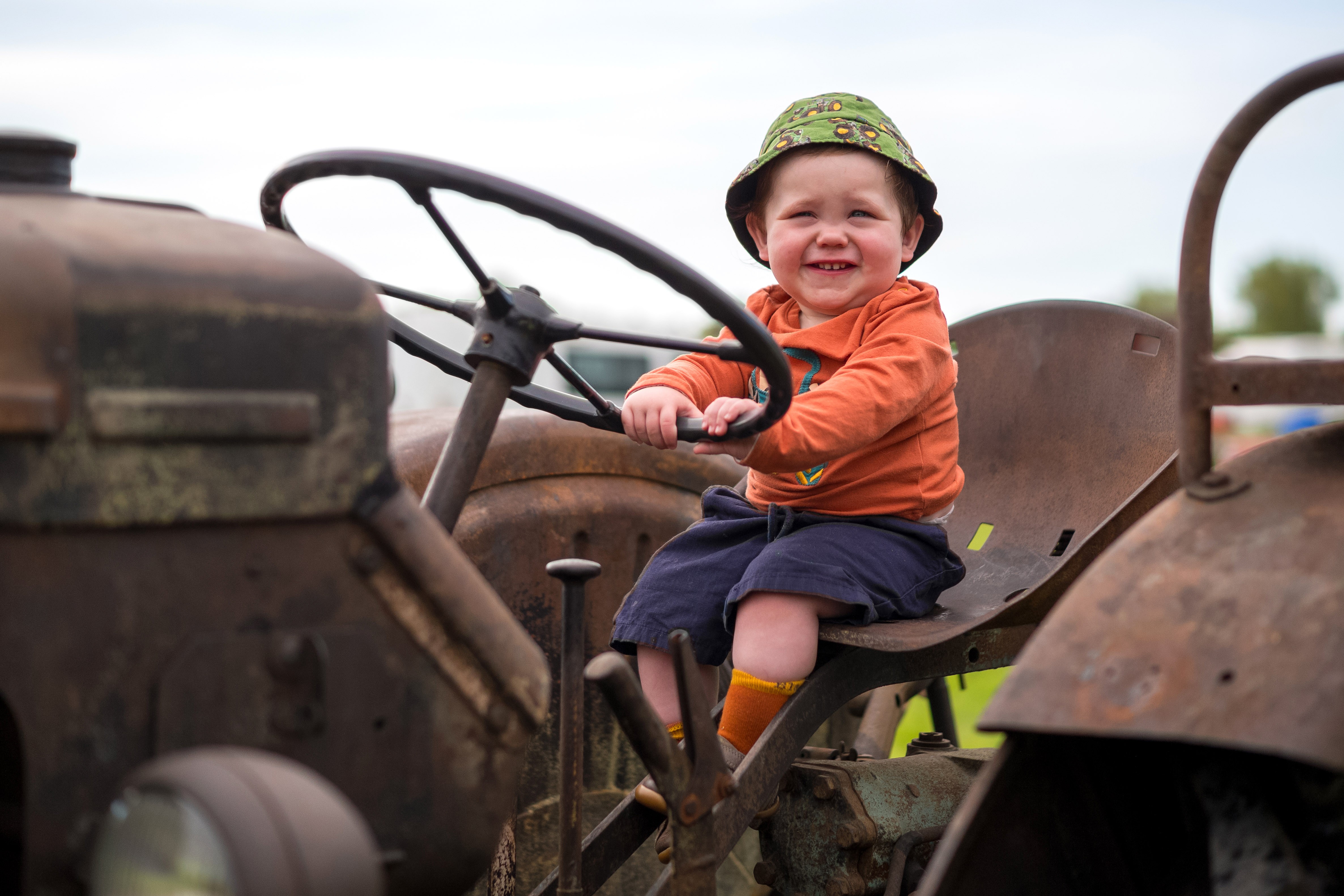 A young boy sits at the wheel of a rusty vintage tractor.