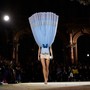 A model walks in a fashion show, wearing a stiff upside-down dress.