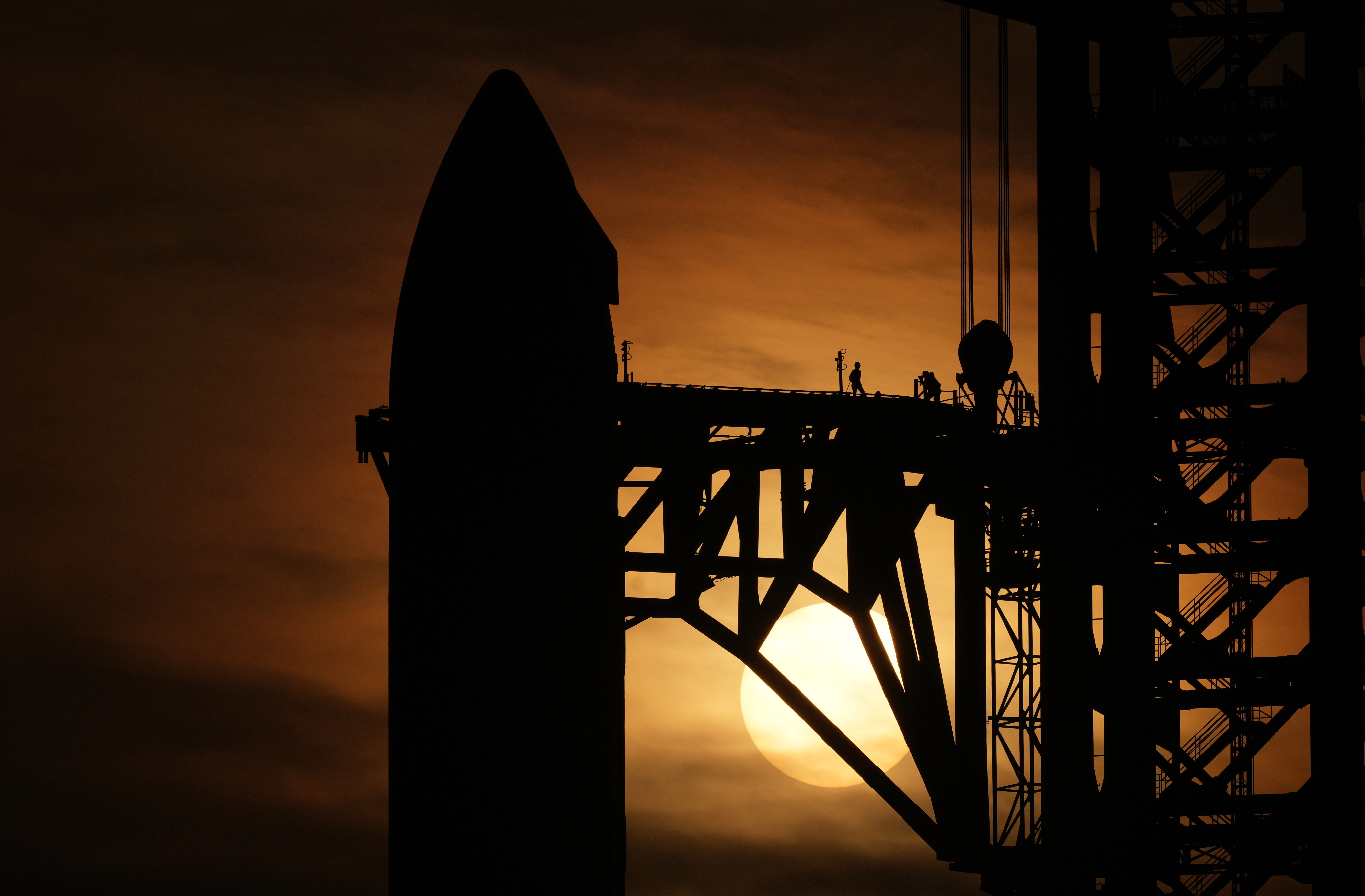 The top of a rocket and its support structure, seen in silhouette at sunset