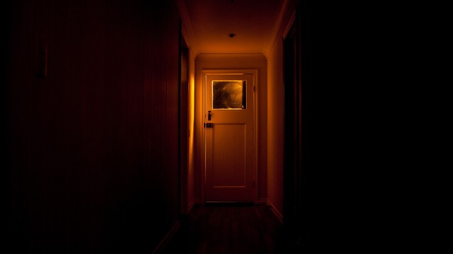 An illuminated door at the end of a dark hallway