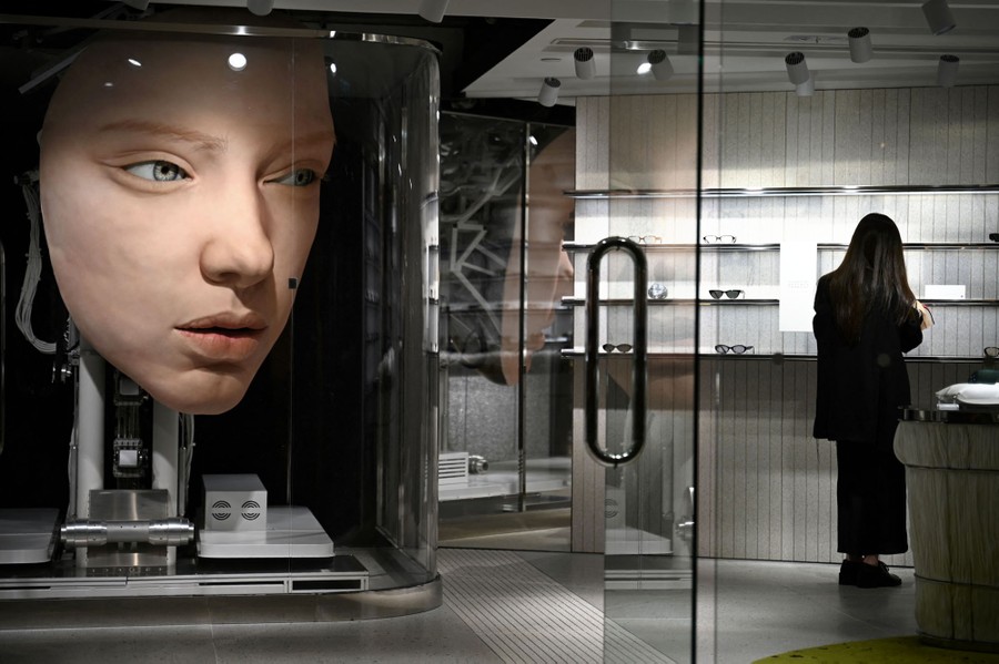 A giant human face sculpture, apparently attached to a mechanical platform, sits behind glass inside a small store.