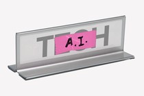 An image of a placard with the text "tech" that is crossed off by tape that reads "AI."