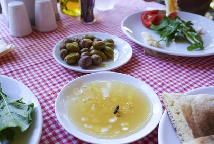 A table set with a checked tablecloth and dishes of food with a plate of honey and a bee in it