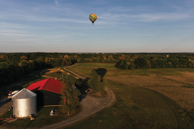 photo of hot-air balloon flying over farm and barn with horizon in distance